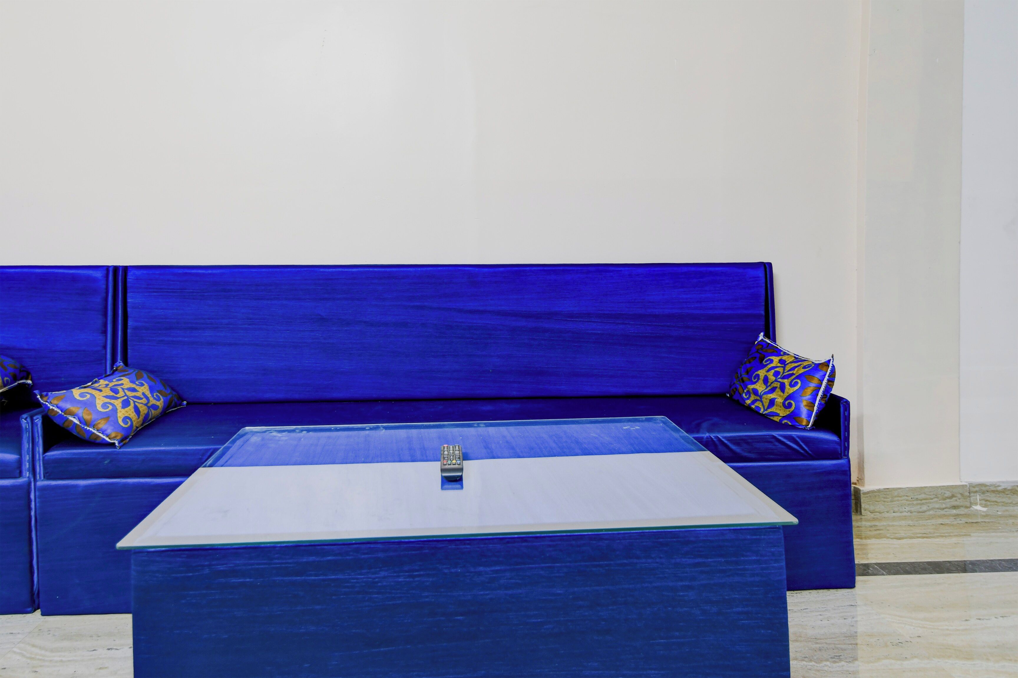 A blue sofa with patterned cushions, a glass-top coffee table, and a marble floor.