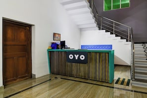 Um balcão de recepção com uma placa indicando 'OYO', uma escadaria e uma porta.
