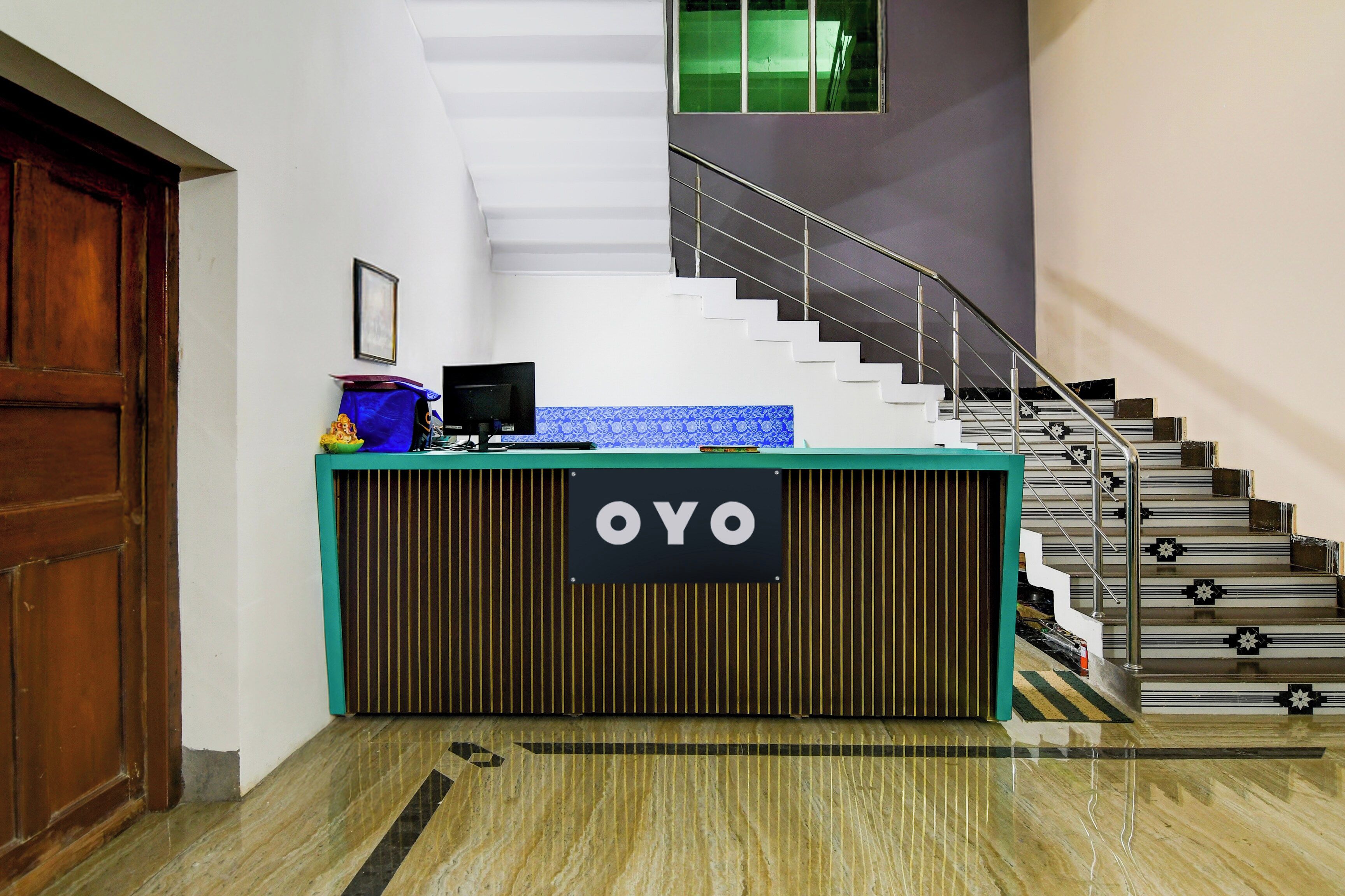 En receptionsdisk med en skylt som visar texten ”OYO” i en hotelllobby med en trappa och en dörr av trä.