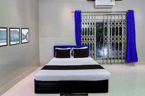 A room with a bed, a window with blue curtains, and three framed pictures on the wall. - Hotel O by OYO Green Eco Space (Kolkata)