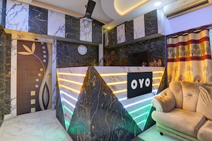 En modern receptionsdisk med en skylt med texten ”OYO”, väggpaneler i marmor, en klocka och en soffa i ett entréområde.