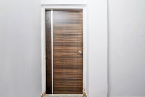 A closed wooden door with a metal handle, set in a white wall with a small step leading up to it. - Hotel O by OYO Acroview (Kolkata)
