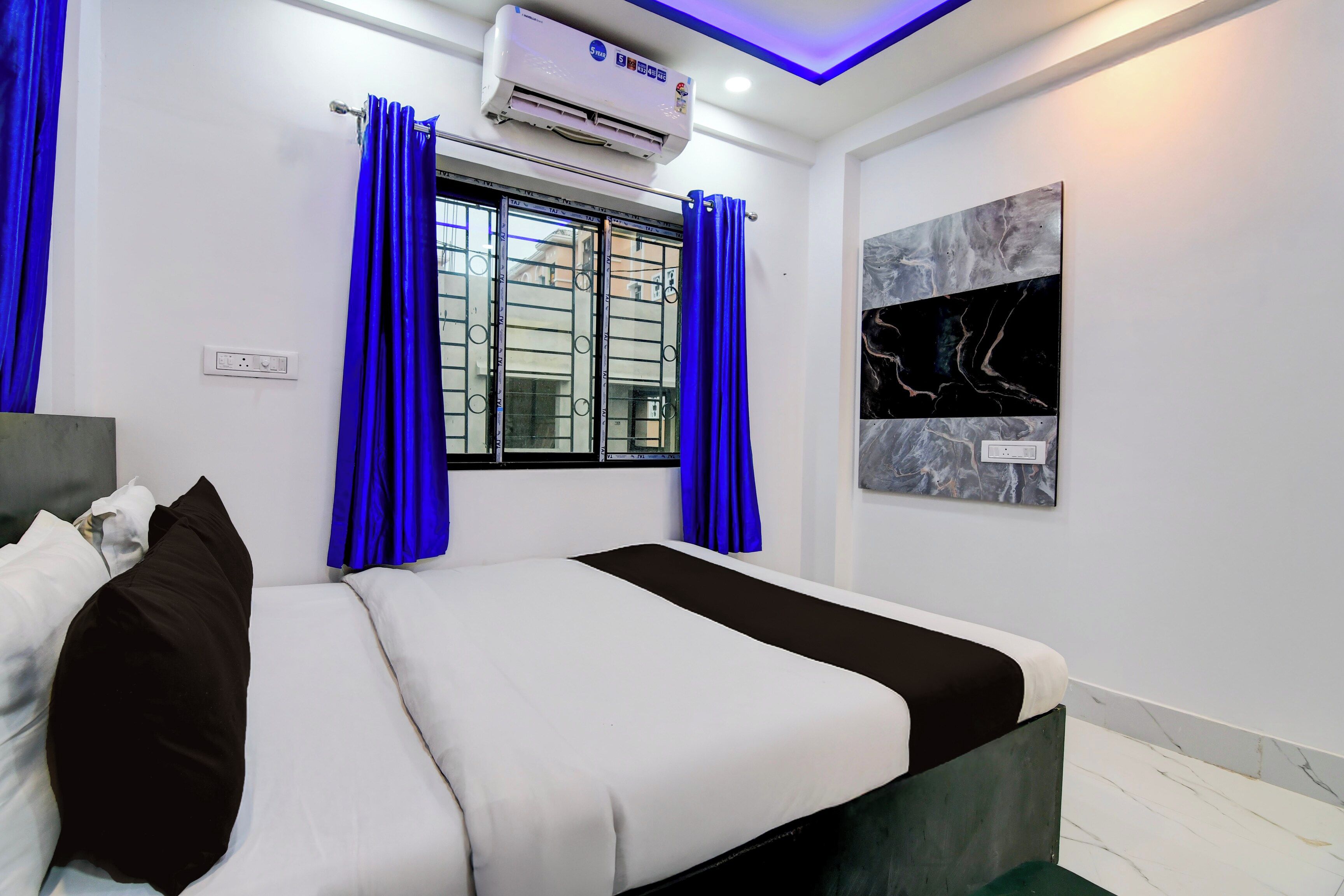 Une chambre à coucher comprenant un lit, des rideaux, un appareil de climatisation et une œuvre d’art accrochée au mur.