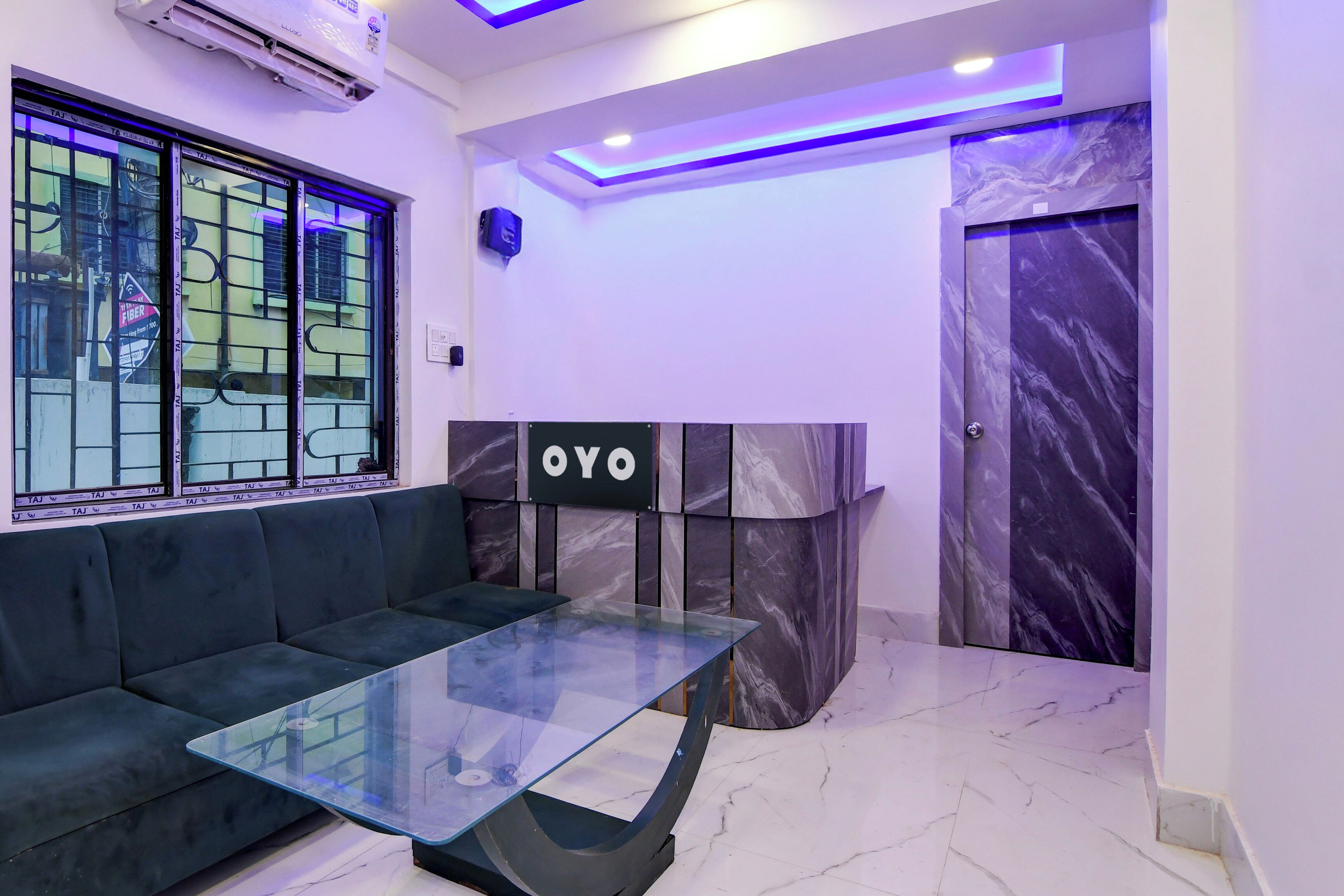 Un intérieur moderne avec un canapé, une table à plateau en verre et un mur en marbre sur lequel est apposée une enseigne indiquant « OYO ».