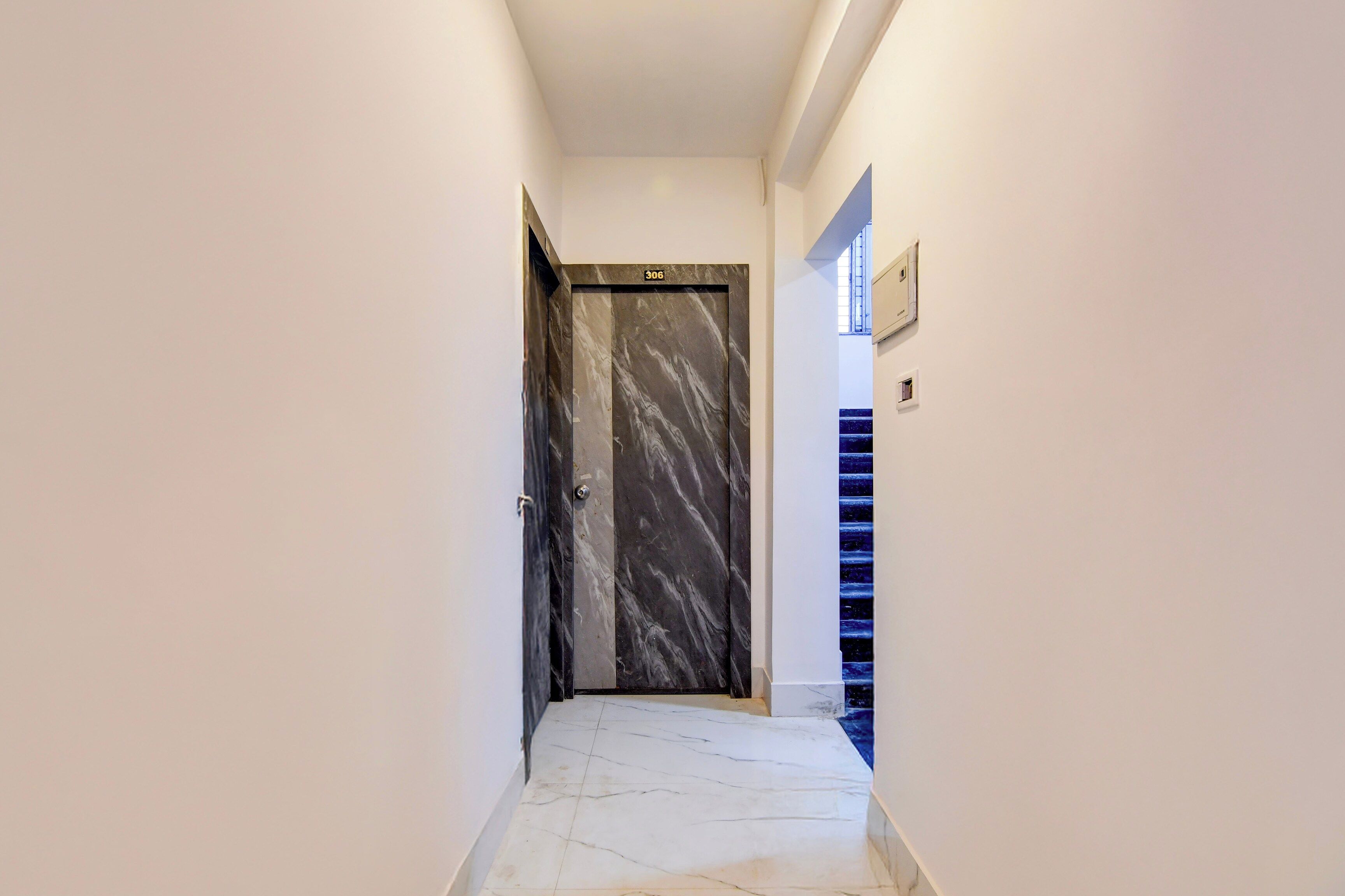 A hallway with a marble floor, a door with a number plate, and a staircase with blue steps.