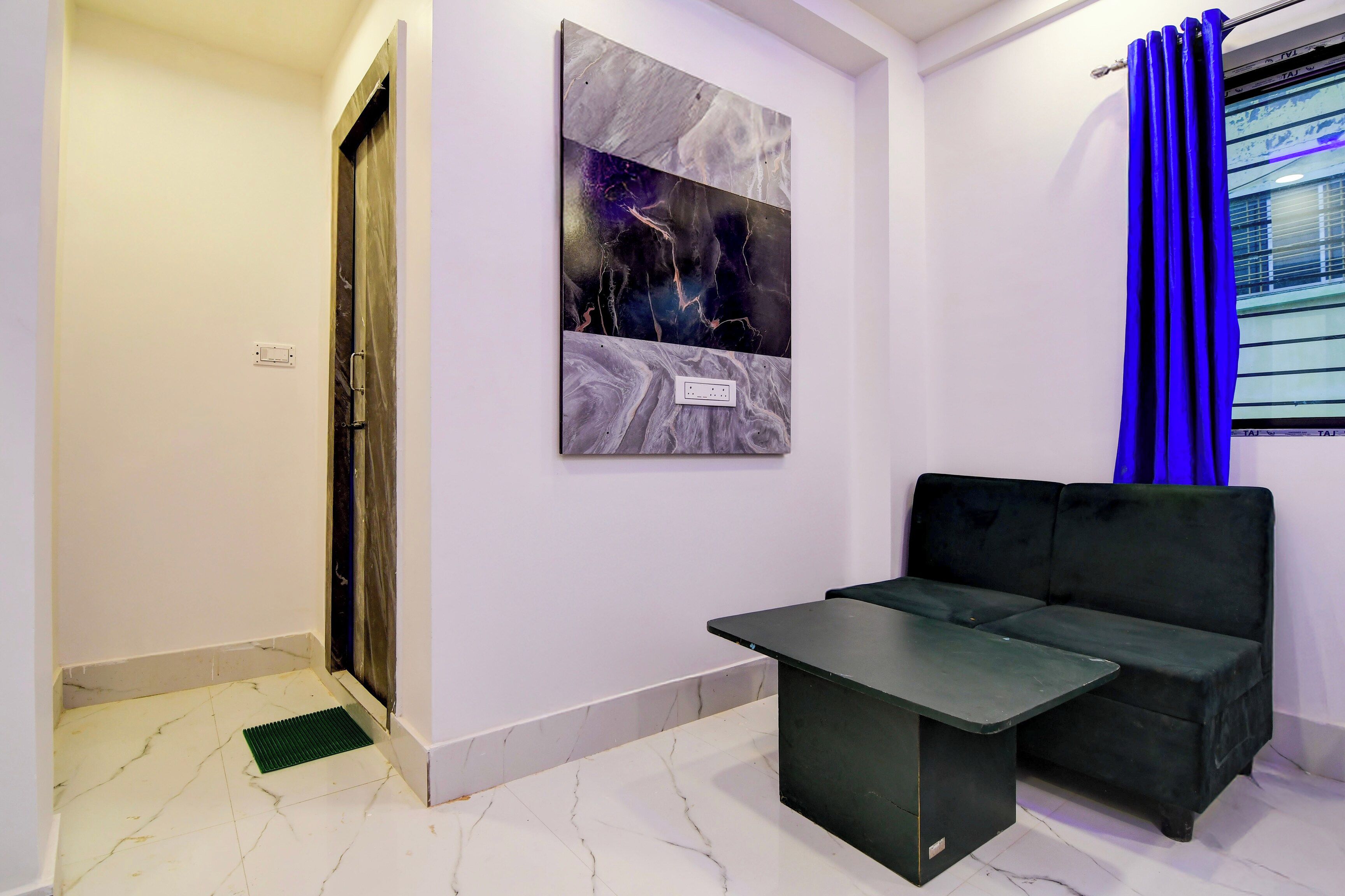 A room with a black sofa, a small table, a wall-mounted artwork, and a window with blue curtains.
