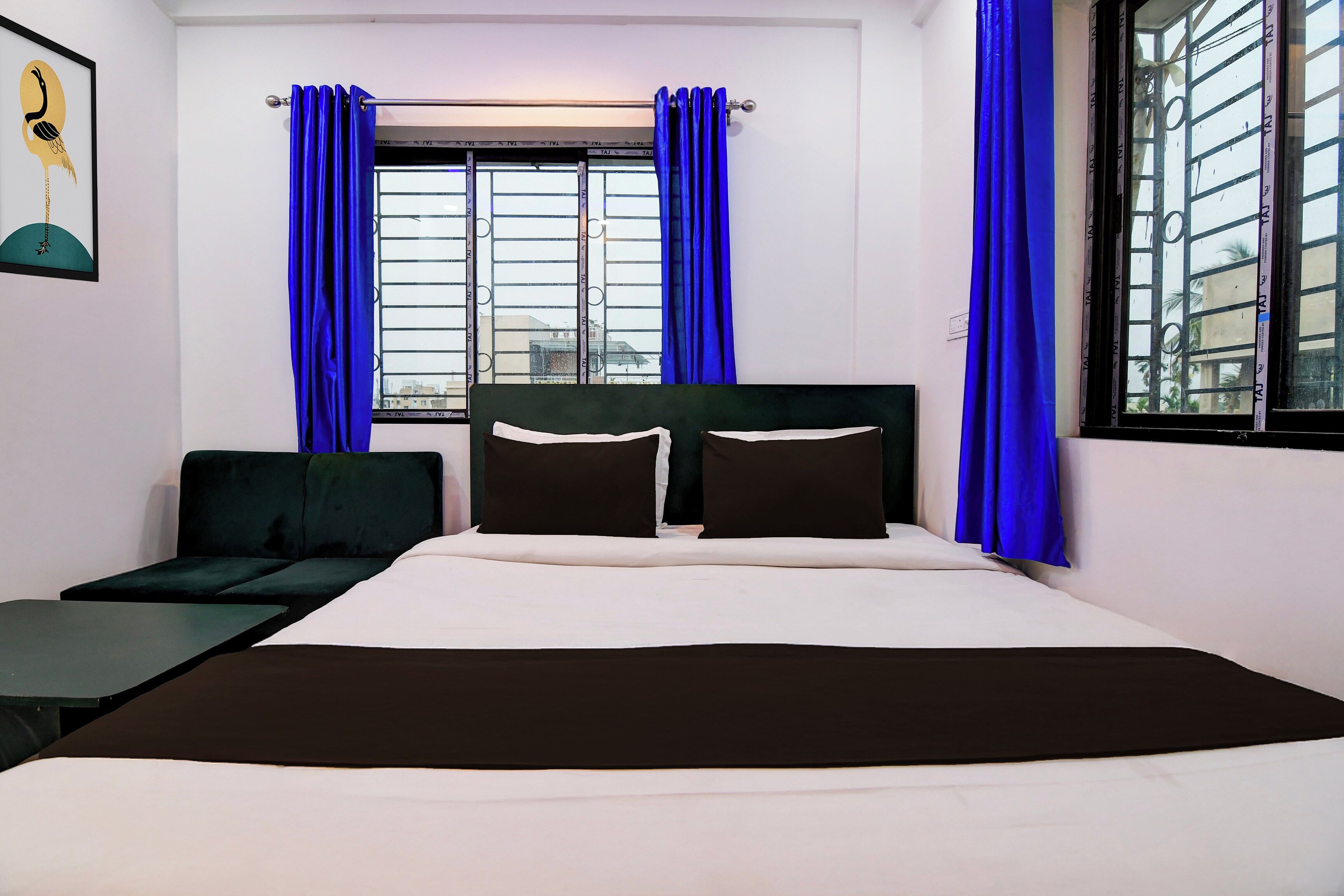 A hotel room with a bed, two pillows, a black headboard, a green sofa, and a window with blue curtains.