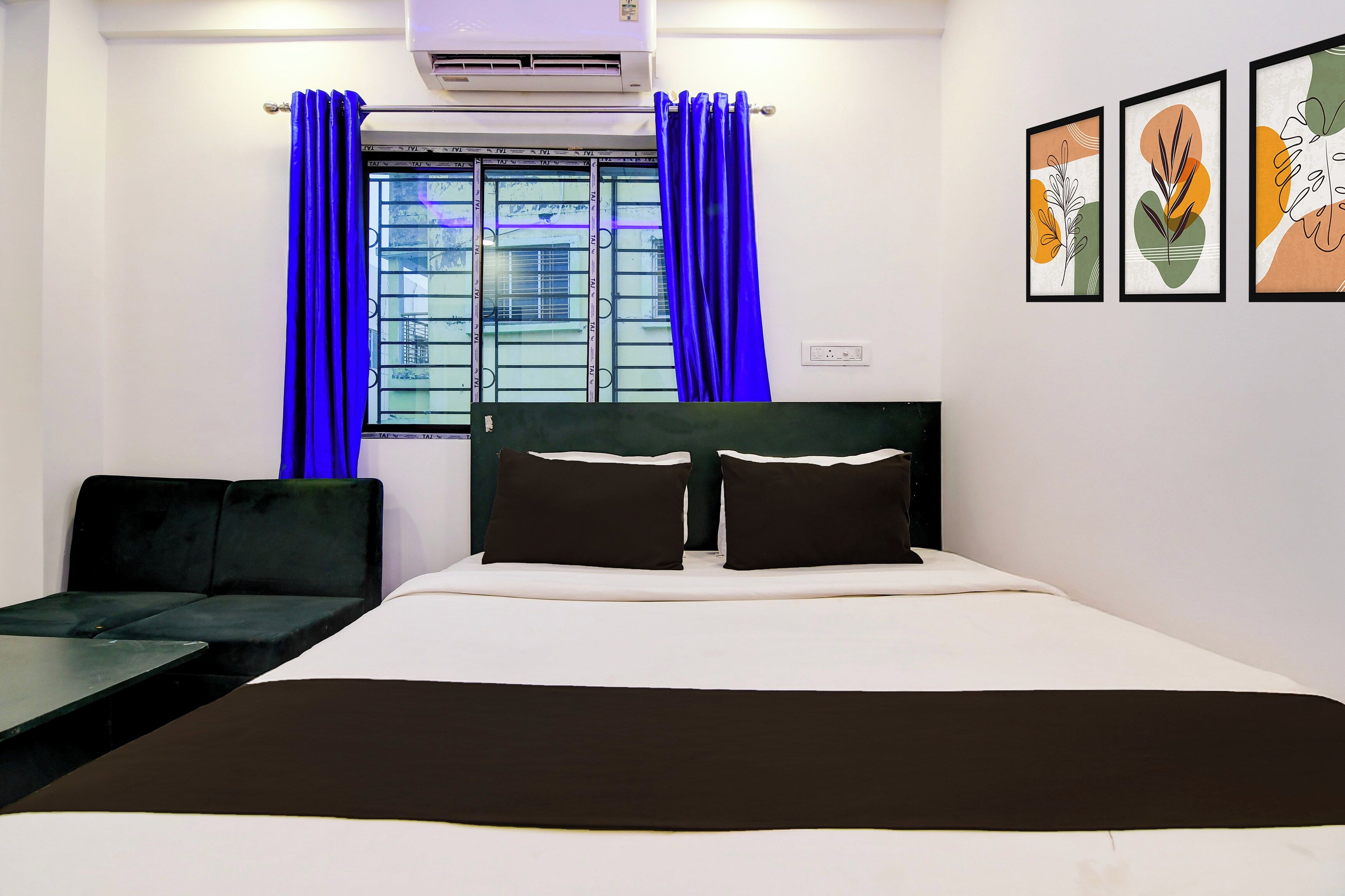 A hotel room with a bed, a sofa, a window with curtains, and wall art.