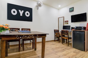 En matplats med ett träbord, stolar, ett litet kylskåp och en tv som är monterad på väggen.