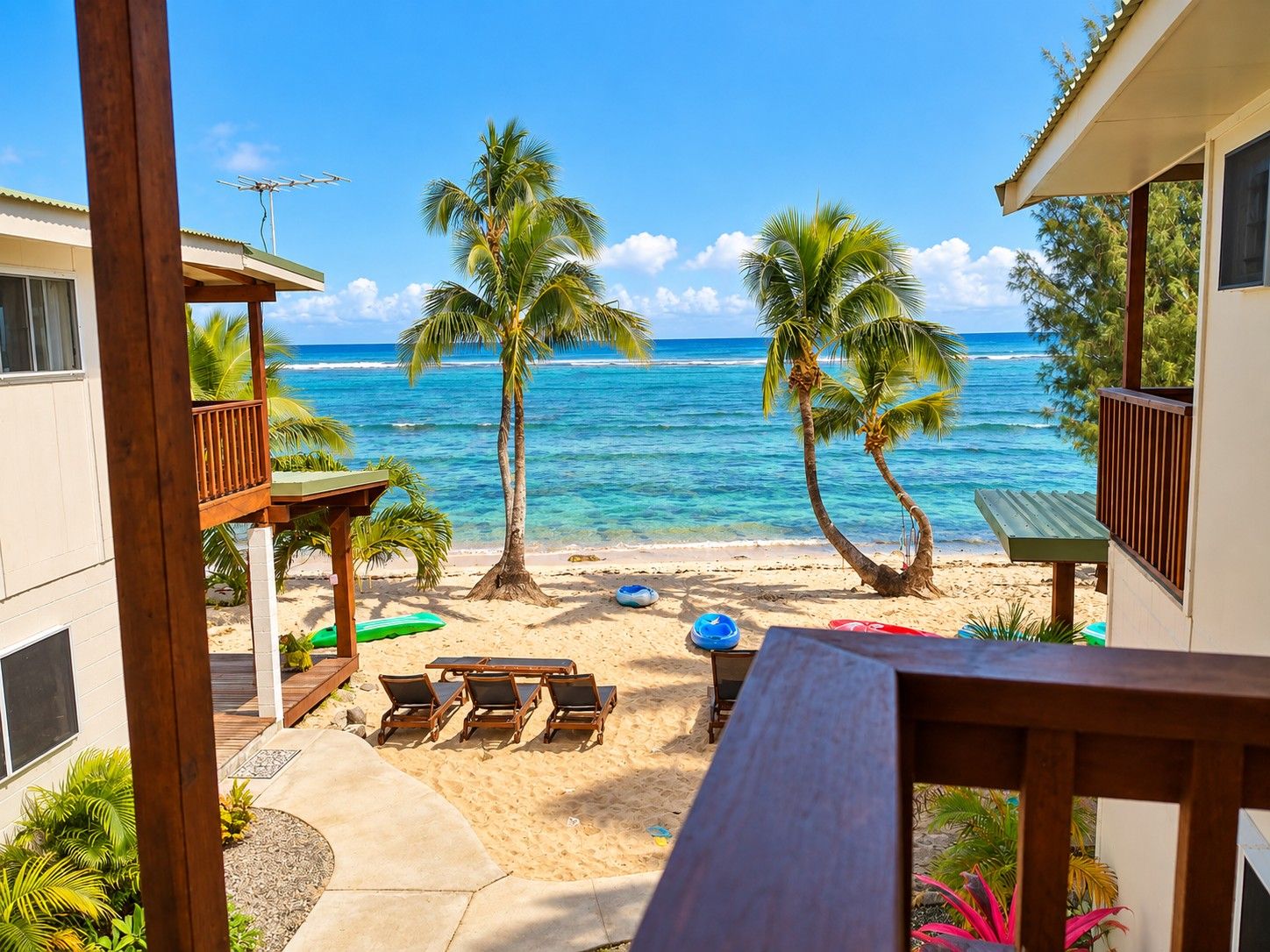 A beach view with a wooden deck, lounge chairs, and a table.