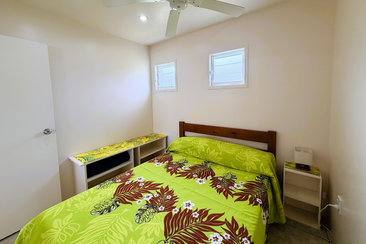 Ein Schlafzimmer mit einem Bett, einem Deckenventilator, einem Fenster und einem Nachttisch.
