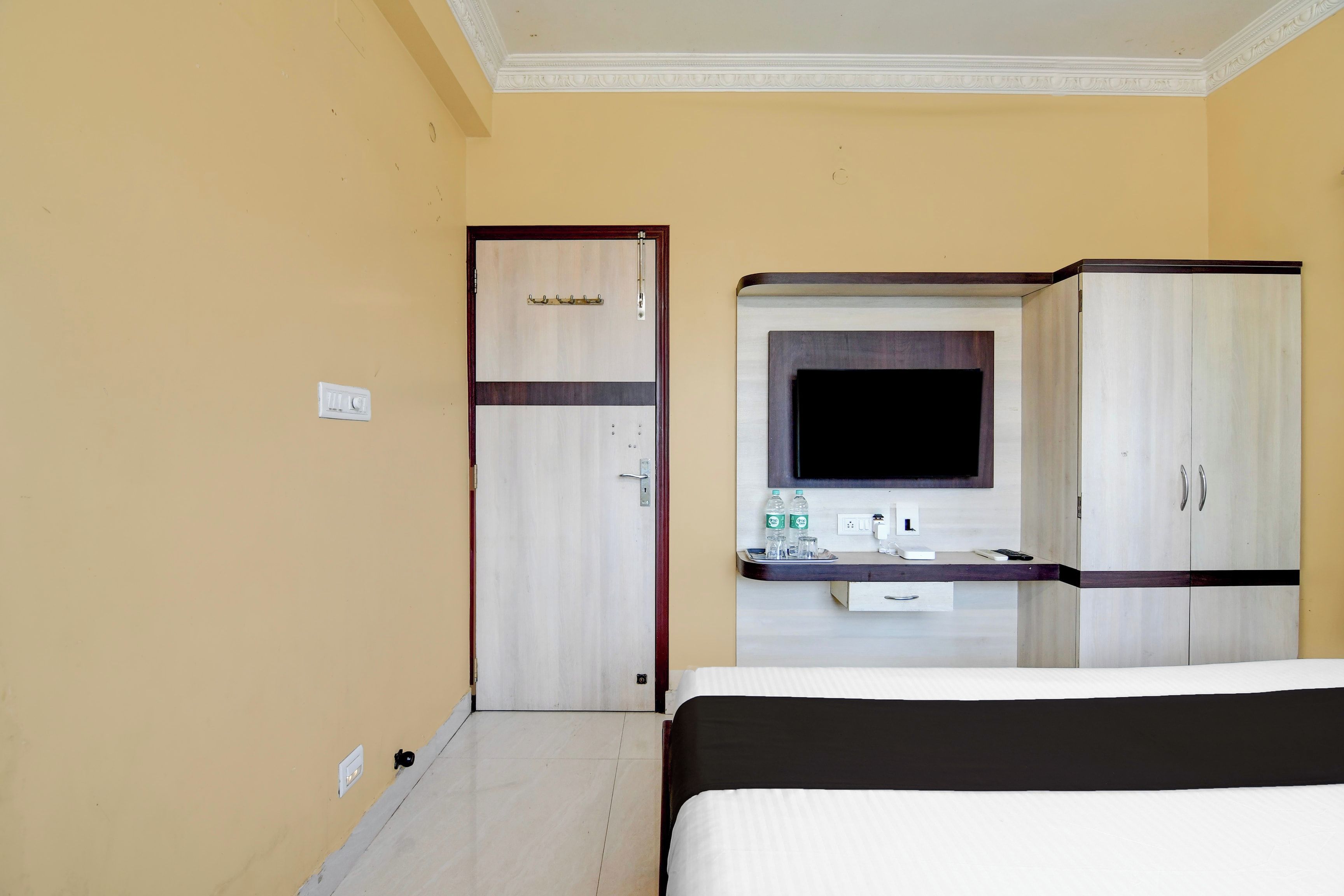A hotel room with a bed, a TV, a minibar, and a door.