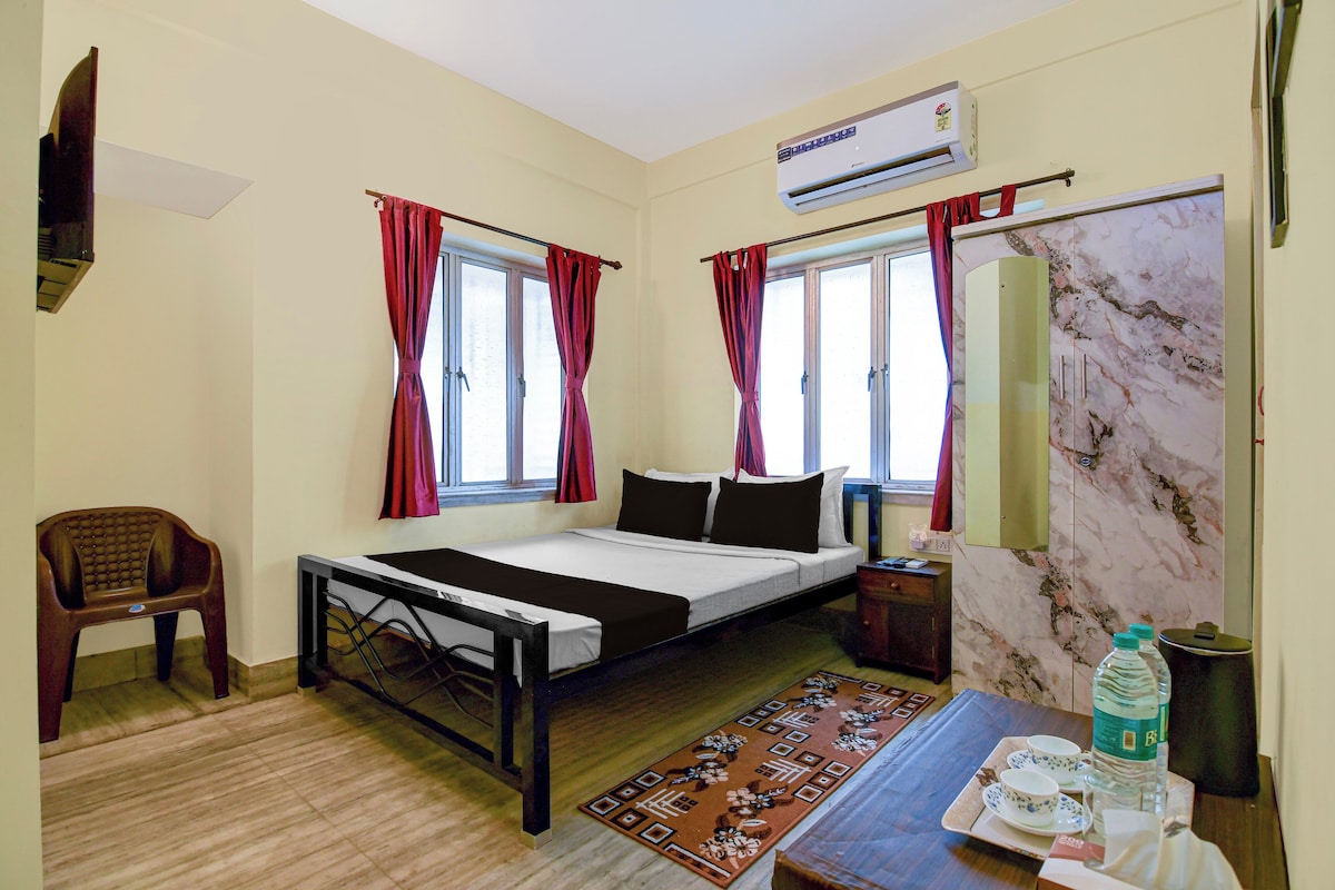 A hotel room with a bed, a desk with a chair, a window with curtains, an air conditioning unit, and a marble-patterned wall.