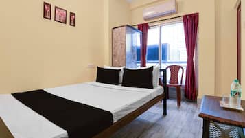 A hotel room with a bed, a chair, a table with a bottle, and a window with curtains.