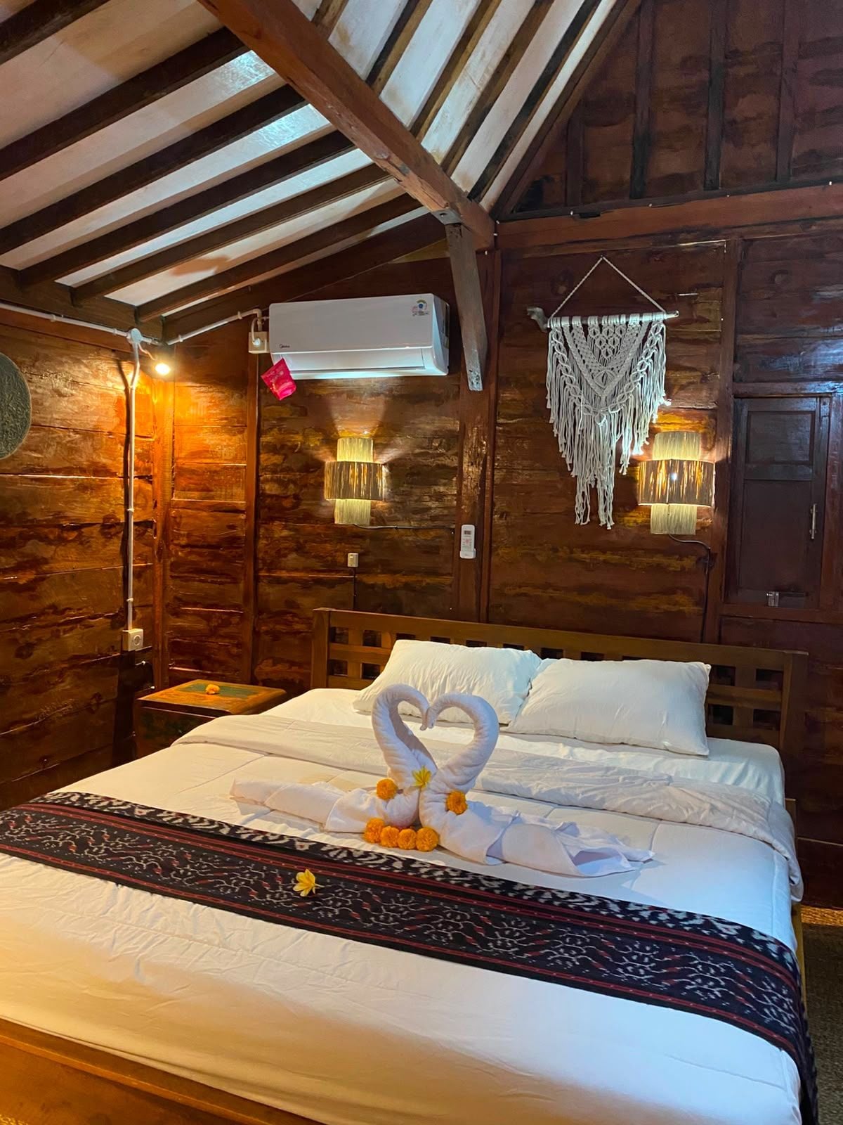 A wooden cabin-style room with a bed, a wall-mounted air conditioner, and a macramé wall hanging.