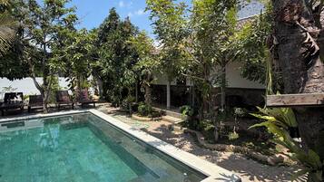 A swimming pool with a stone border, surrounded by trees and a house in the background.