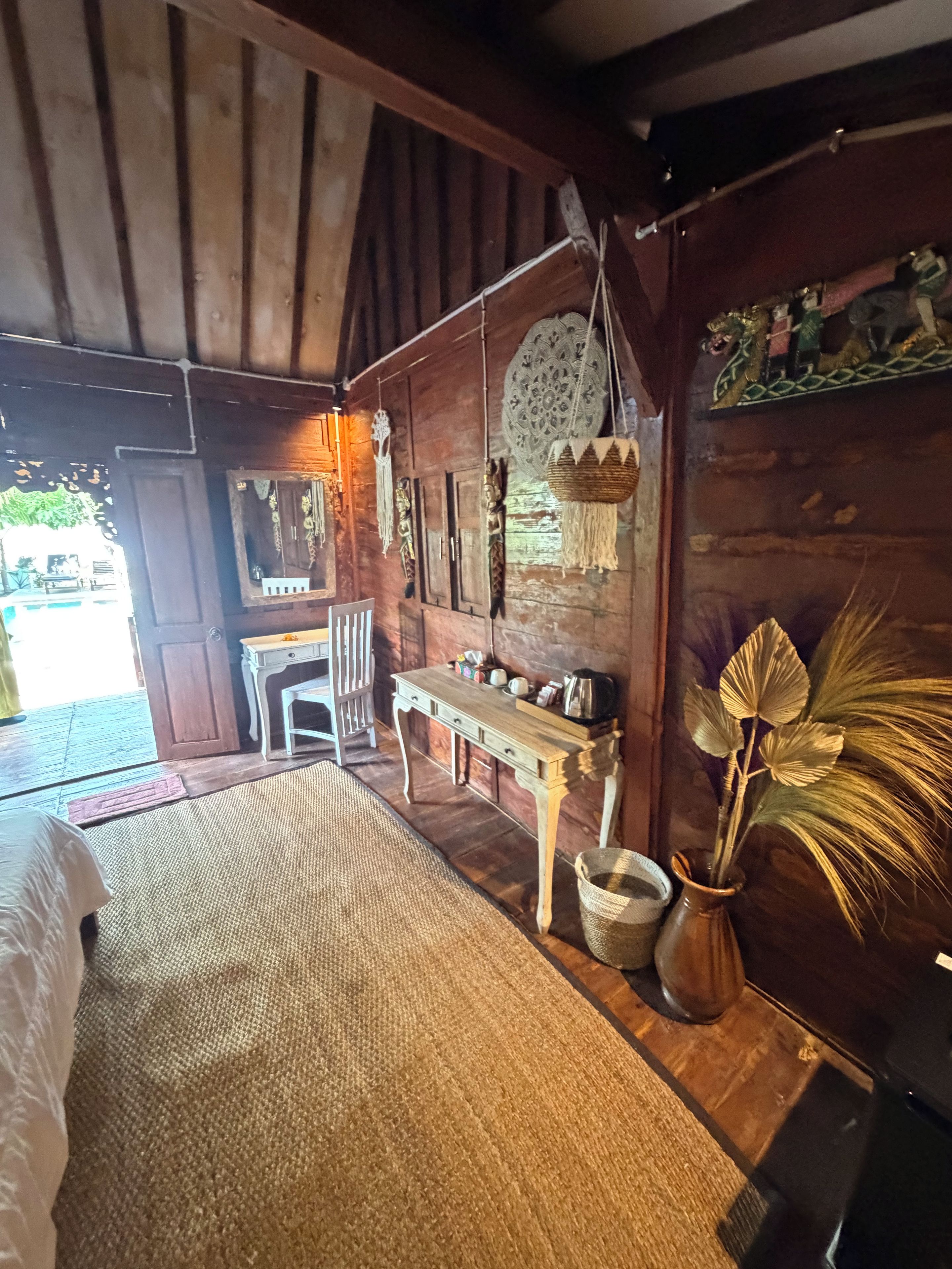 A rustic wooden room with a bed, a small table, and a hanging decorative item.