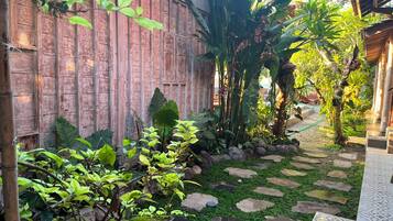 Un jardín con cerca de madera, plantas tropicales y un sendero de piedra.