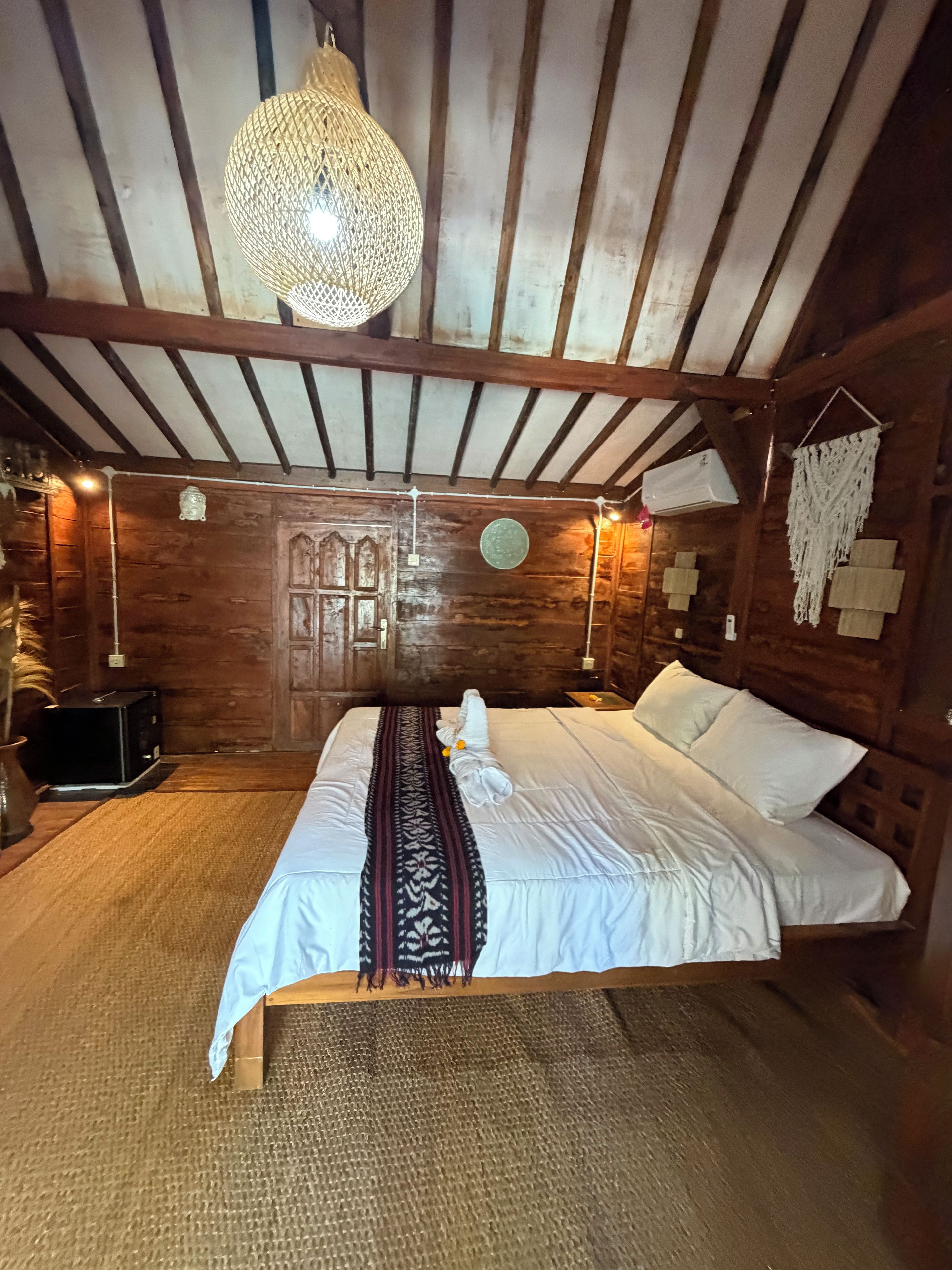 A wooden room with a bed, a hanging light fixture, and a wall-mounted air conditioner.