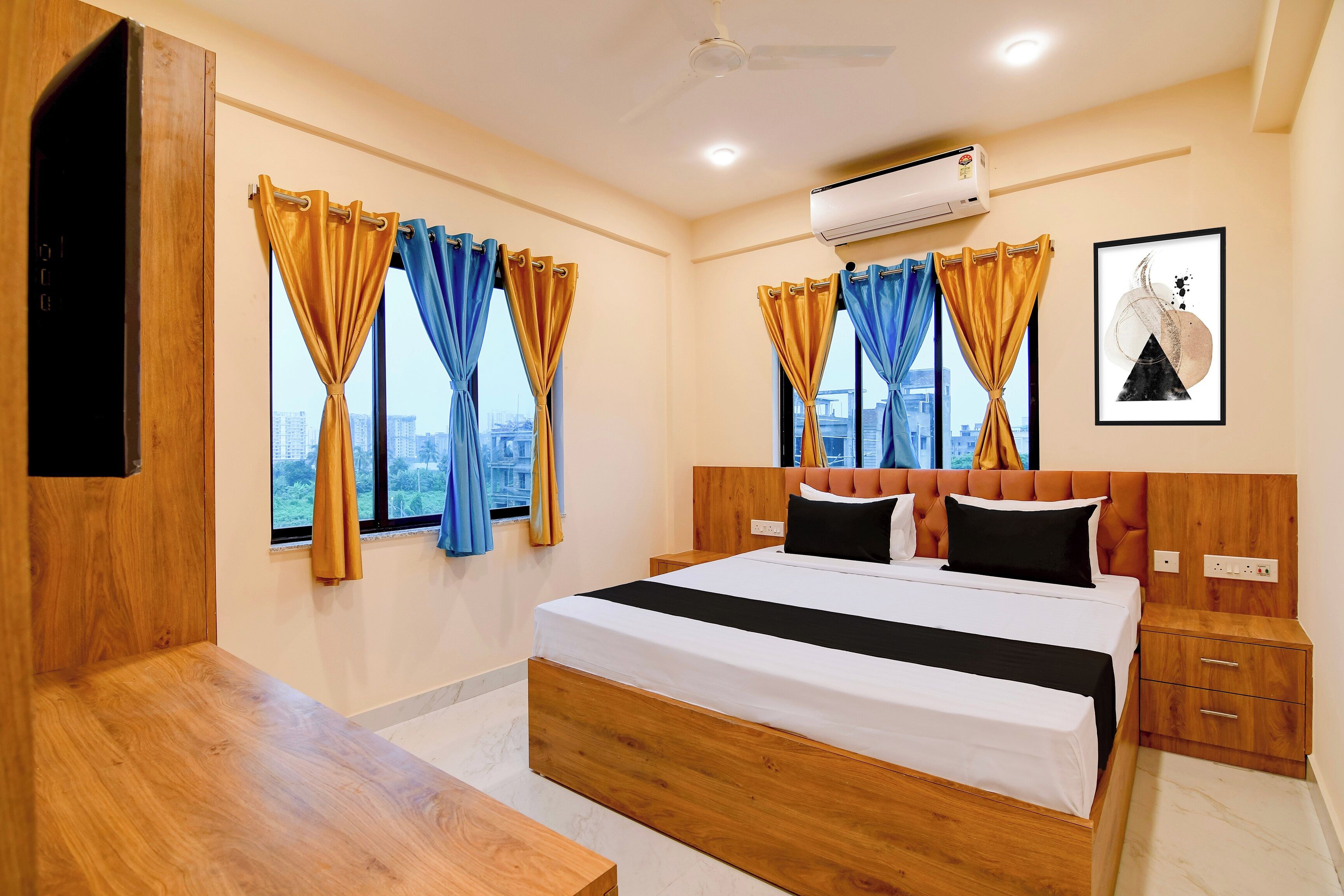 A hotel room with a bed, bedside tables, an air conditioning unit, and a city view.