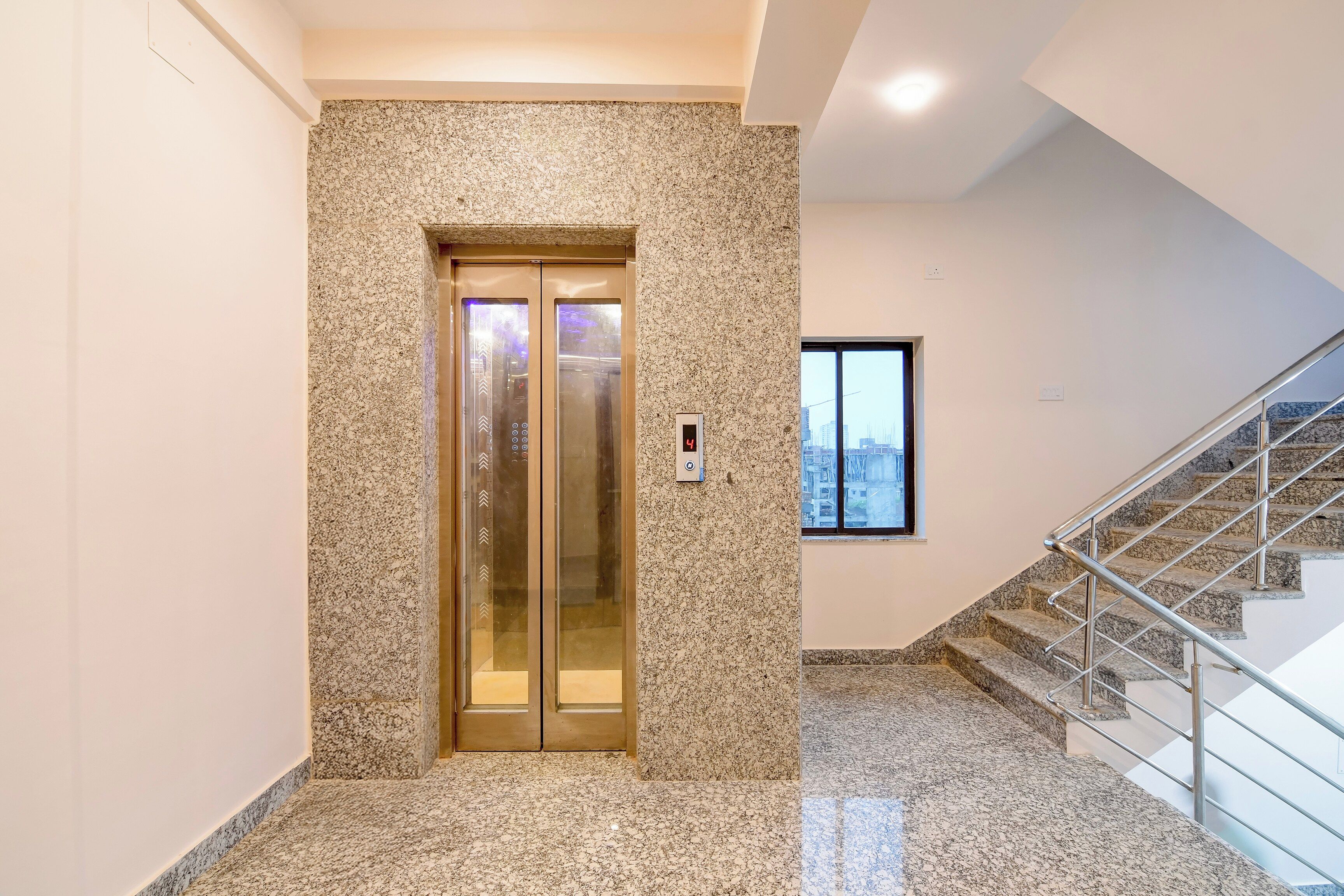 An elevator with a granite wall, a digital display, and a staircase with metal railings.