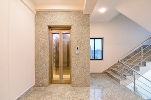 An elevator with a granite wall, a digital display, and a staircase with metal railings. - Hotel O NamaStay (Barasat)