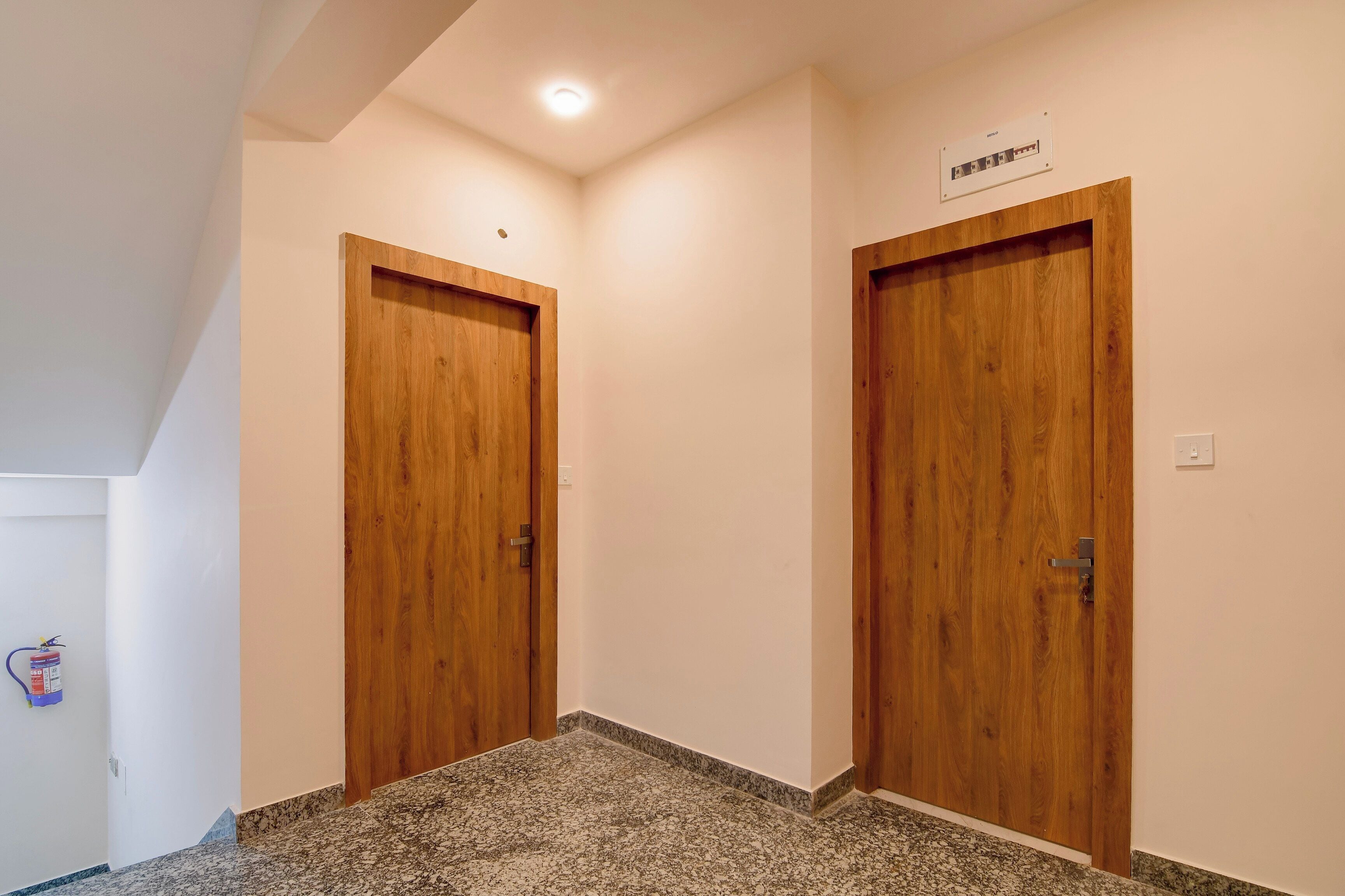 A hallway with two wooden doors, a ceiling light, and a fire extinguisher on the wall.