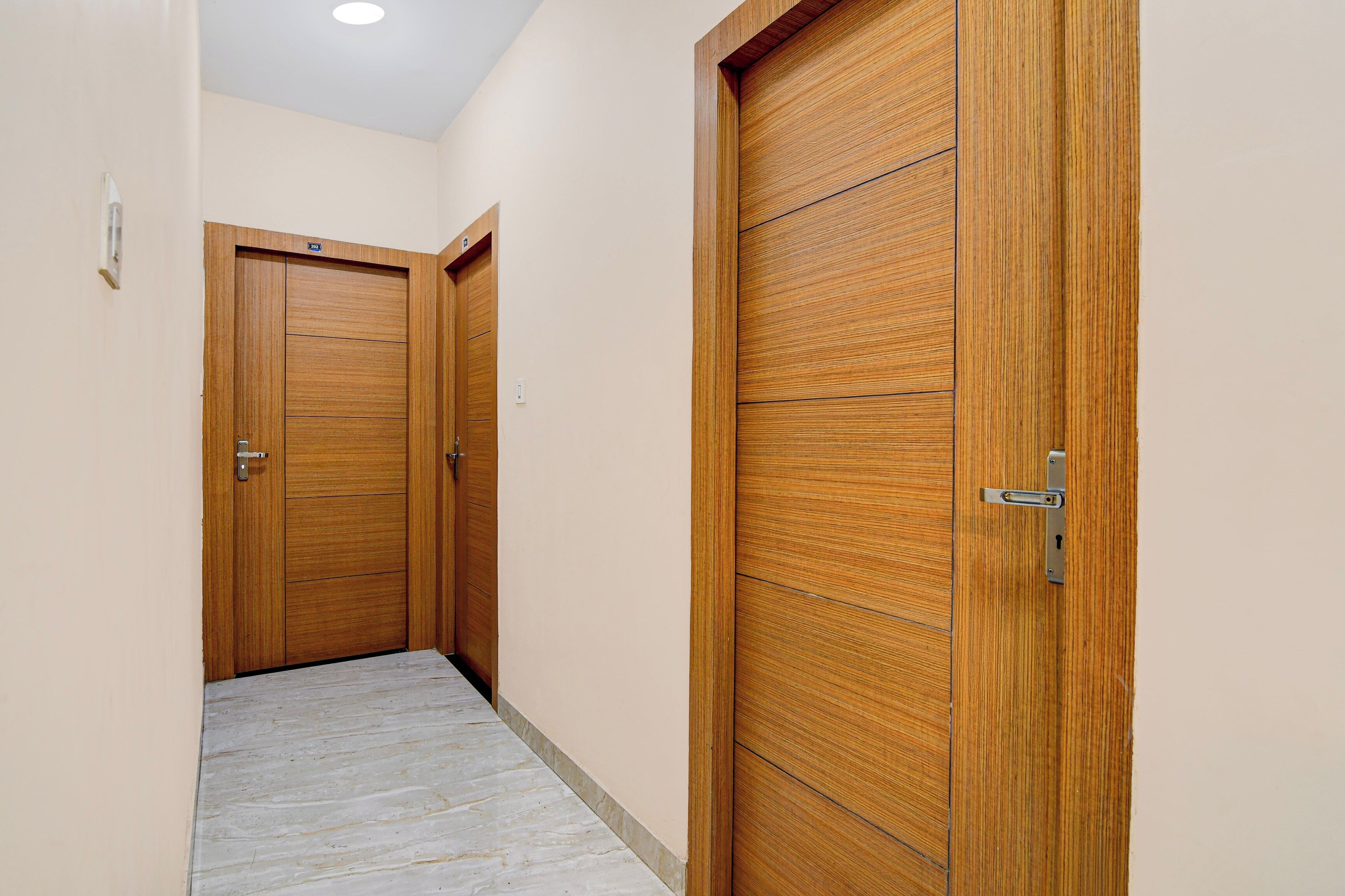 Un pasillo con puertas de madera, suelo de baldosas y una lámpara en el techo.