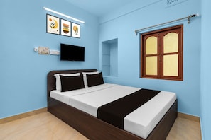 A bedroom with a bed, a flat-screen TV, a window with wooden shutters, and wall-mounted artwork. - Hotel O Krivaan Guest House (Kolkata)