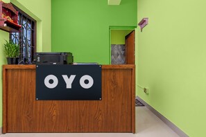 Un mostrador de recepción con un cartel que dice 'OYO' en el vestíbulo de un hotel con paredes verdes y un mostrador de madera.