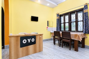 En receptionsdisk med en skylt som visar texten ”OYO” i ett rum med gula väggar, ett matbord med stolar och ett fönster med gardiner.