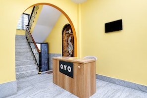 En receptionsdisk med OYO-logotyp, en trappa med ett svart räcke och en gul vägg.