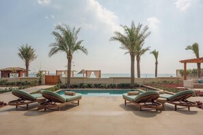 Ein Poolbereich mit Liegestühlen, Palmen und Blick auf das Meer.