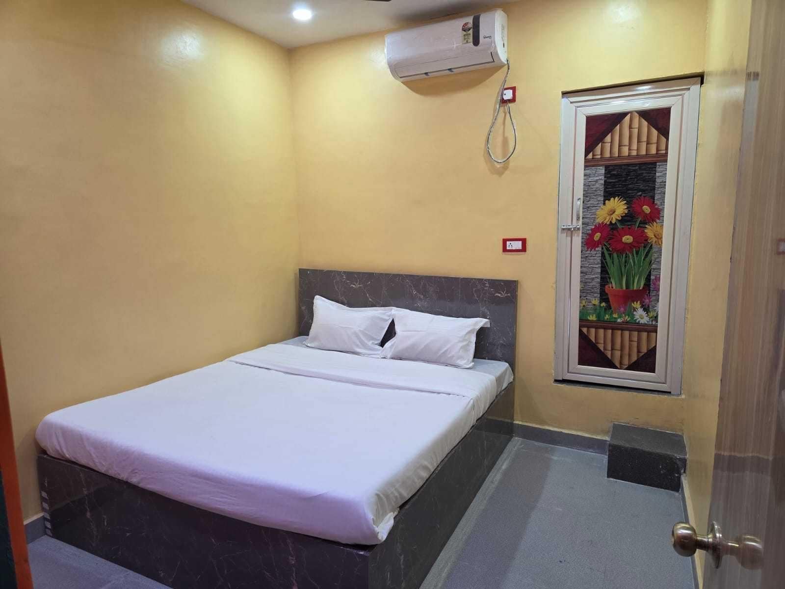 A hotel room with a bed, an air conditioning unit, a window with a floral design, and a door.