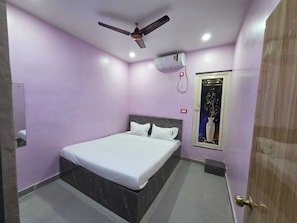 A bedroom with a bed, a ceiling fan, an air conditioning unit, a door, and a wall-mounted light switch. - Hotel O Highway Horizon Inn (Kolkata)