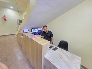 Ein Empfangsschalter mit einem Computermonitor, ein Feuerlöscher an der Wand und eine Treppe, die in eine obere Ebene führt.