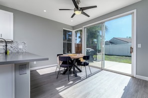 A modern kitchen with a built-in island, a dining area with a table and chairs, and a sliding glass door leading to a backyard. - Elegant Menifee Lakes Retreat with Pool and Spa (Menifee)