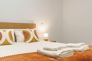Uma cama bem arrumada com almofadas, um abajur e toalhas dobradas.
