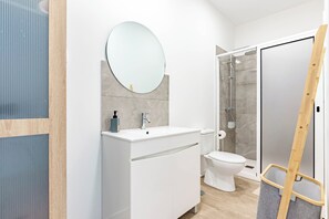 Un baño moderno con tocador blanco, un espejo redondo, un inodoro y una zona de ducha.