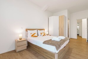 Un dormitorio moderno con cama de madera, ropa de cama blanca y una mesita de noche con lámpara.