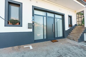 Un bâtiment moderne doté d’une grande porte vitrée, d’une petite plante en pot et d’un escalier menant à l’entrée.