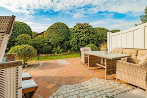 An outdoor patio with wicker furniture, a stone-tiled floor, and lush greenery in the background. - Holiday apartment with 2 bedrooms (Braderup)