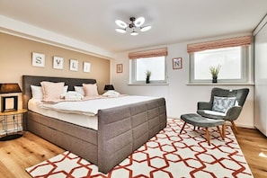 A bedroom with a bed, bedside tables, a chair, windows, and a ceiling fan. - Holiday apartment with 2 bedrooms (Braderup)