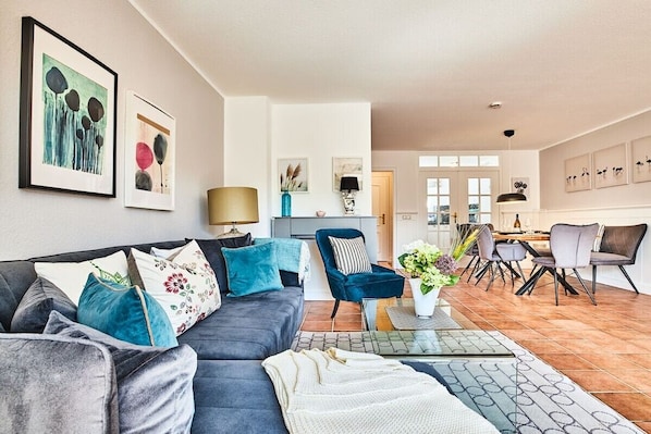 A modern living room with a sofa, coffee table, and dining area with chairs. - Holiday apartment with 2 bedrooms (Braderup)