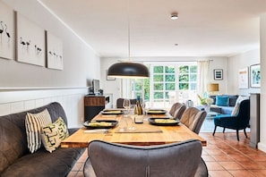 A dining area with a wooden table set for four, a sofa, and a television on a stand. - Holiday apartment with 2 bedrooms (Braderup)