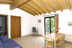 A room with a wooden ceiling, a dining table with chairs, a television, and a sliding glass door leading to a balcony. - Apartments Cepo, Pieve di Tremosine (Tremosine)