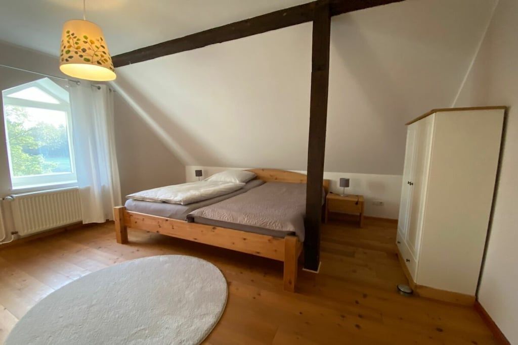 Une chambre à coucher avec un lit en bois, une armoire blanche et un luminaire suspendu.