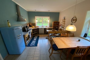 A compact kitchen with a blue refrigerator, wooden dining table, and a window with a view of greenery. - Rehwinkel Forestry House (Südheide)