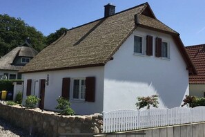 A white house with a thatched roof and a stone wall in front. - Thatched holiday home with sauna (Koserow)