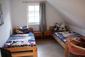 A dormitory room with two single beds, a wooden chair, a desk, and a window with curtains. - Thatched holiday home with sauna (Koserow)